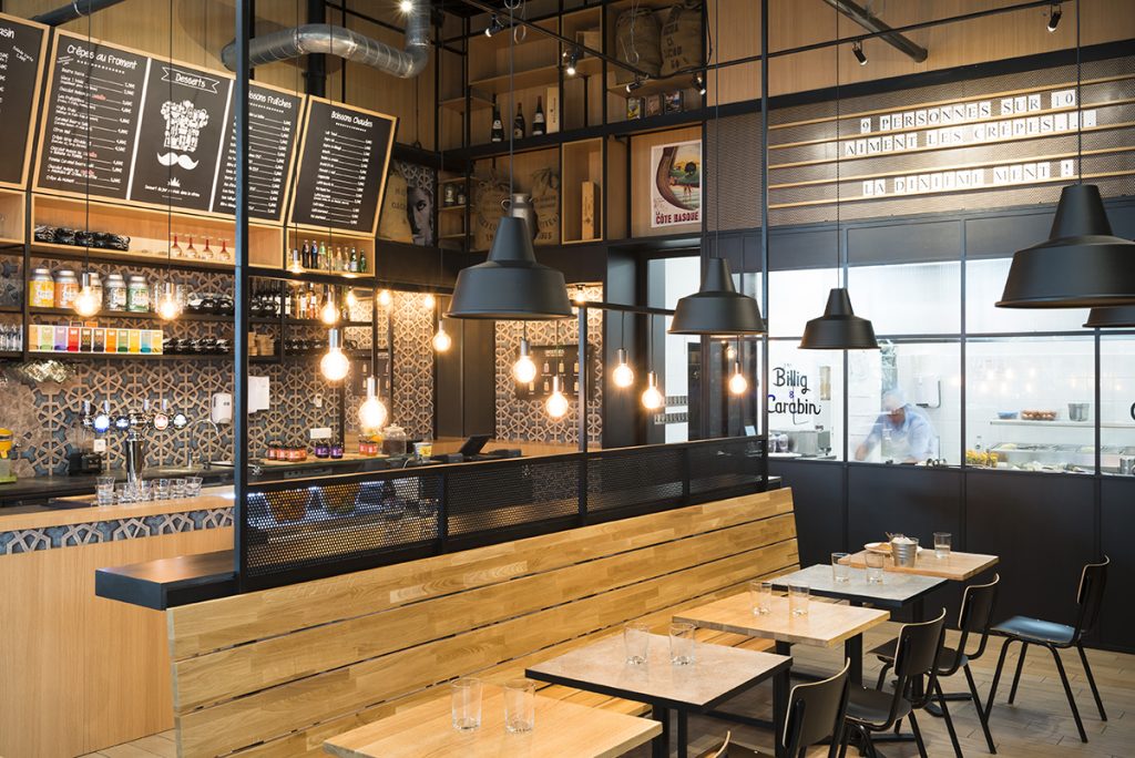 Intérieur du restaurant Billig & Carabin — comptoir, lampes industrielles, banquettes en bois et cuisine ouverte